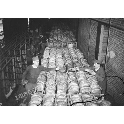 Des soldats rangent des boules de pains dans de vastes paniers métalliques.