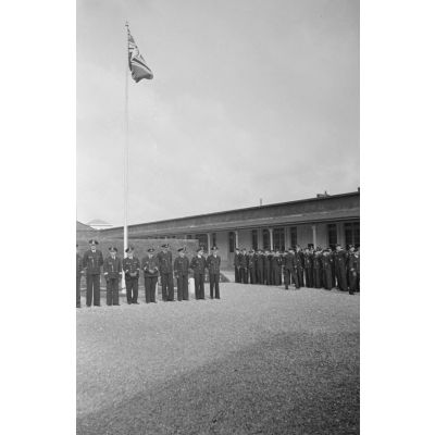 Lors d'une cérémonie de la Kriegsmarine à Saint-Nazaire, des sous-officiers se tiennent au garde-à-vous devant le mat des couleurs orné du drapeau à croix gammée.