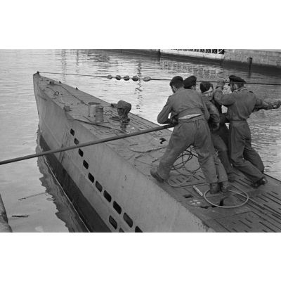 Des membres de l'équipage d'un U-Boot éloignent le submersible du quai pour l'aligner et débarquer le personnel comme le matériel.
