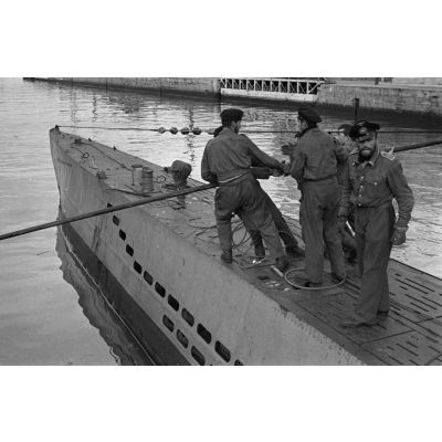 Des membres de l'équipage d'un U-Boot éloignent le submersible du quai pour l'aligner et débarquer le personnel comme le matériel.