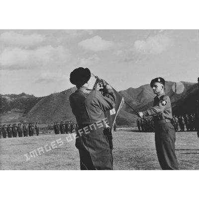 [Le général Monclar décore le fanion du bataillon français de l'ONU porté par le commandant Maurice Barthélemy.]