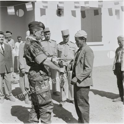 [Le général de brigade Jacques Massu remet un fusil à un Algérien, 1956-1958.]