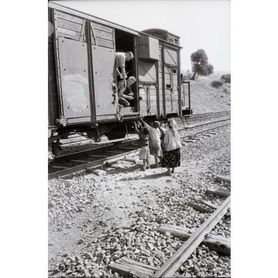 [Deux hommes à bord d'un wagon distribuent des vivres à de jeunes Algériens, 1958-1961.]