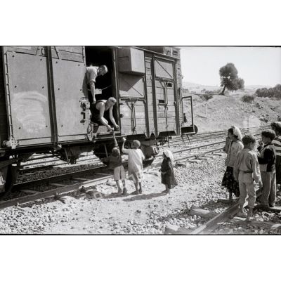 [Deux hommes à bord d'un wagon distribuent des vivres à de jeunes Algériens, 1958-1961.]