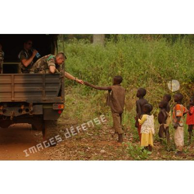 A bord d'un véhicule, un militaire donne une friandise à un enfant.