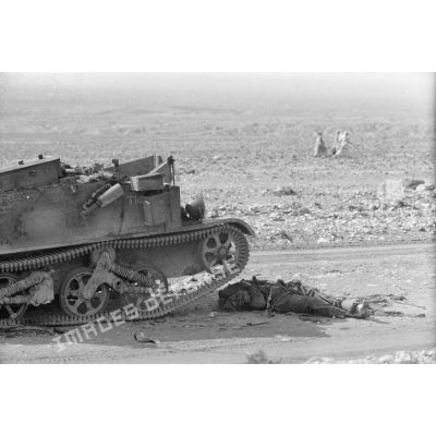 Un cadavre britannique gît au pied d'un blindé Universal Carrier détruit.
