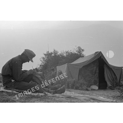 Un membre d'équipage d'un blindé Panzer III (non visible) fait des travaux de réparation près de sa tente en partie camouflée.