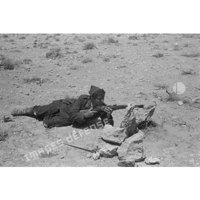 Un bersaglier est allongé en position de tir derrière des pierres, il est armé d'un fusil Carcano M91/38 TS.
