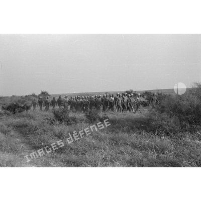Une unité allemande (peut-être des artilleurs) marche, en ordre serré, sous la conduite d'un officier, au milieu des buissons.
