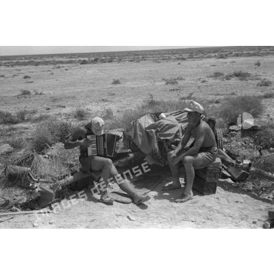 Un soldat joue de l'accordéon sur une flèche d'un canon antichar 5 cm PaK 38, sous le regard d'un camarade.