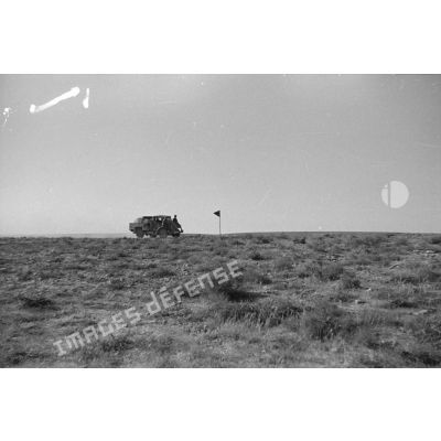 Un camion Morris 15 cwt d'origine britannique roule dans le désert près d'un fanion d'unité.