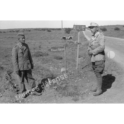 Un soldat et un Oberleutnant posent près de deux panneaux indiquant la localisation d'unités de la 21-Pz.Div.