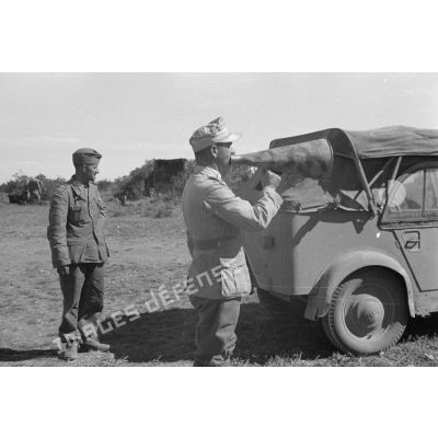 Un lieutenant (Oberleutnant) donne des ordres à l'aide d'un porte-voix près d'un homme de troupe et d'une voiture Kfz-1.