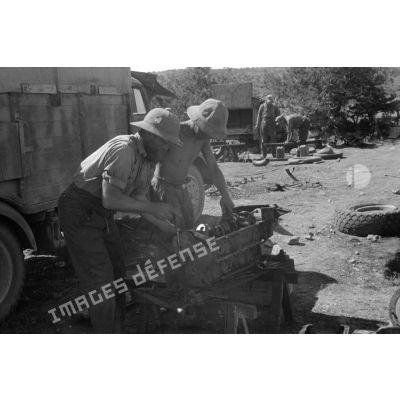 Deux soldats, coiffés du casque colonial, assurent la maintenance de pièces mécaniques.