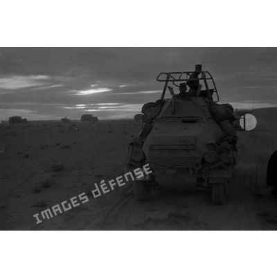Un blindé SdKfz-263 roule dans le désert au crépuscule au milieu d'une colonne de véhicules.