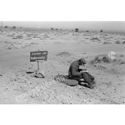 Panneau de signalisation (Einfahrt zur Reifenstaffel). Un soldat lit assis sur un pneu.