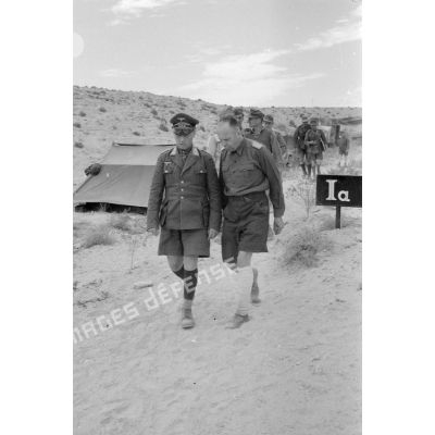 Les généraux Rommel et von Ravenstein marchent en parlant devant des tentes et un panneau marqué Ia (Etat-major divisionnaire).