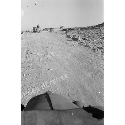 Une colonne de véhicules roule sur la via Balbia, elle dépasse un char britannique Matilda Mark-II détruit.