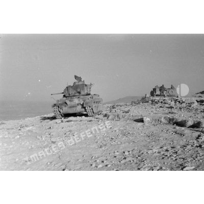 Une colonne de véhicules roule sur la via Balbia, elle dépasse un char britannique Matilda Mark-II détruit.