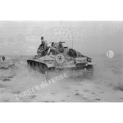 Un char Panzer III (Pz-III), dont deux hommes d'équipages sont à l'extérieur, transporte deux prisonniers britanniques.