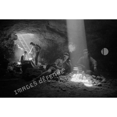Deux soldats utilisent un téléphone de campagne à l'intérieur d'une grotte où filtre un rayon de lumière.