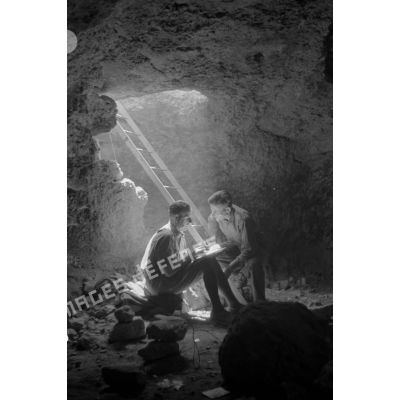 Deux officiers discutent près de l'entrée de la grotte qui consiste en une échelle.