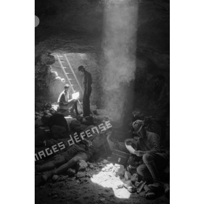 Deux soldats utilisent un téléphone de campagne dans la grotte sous un rayon de lumière. L'un d'eux fume.
