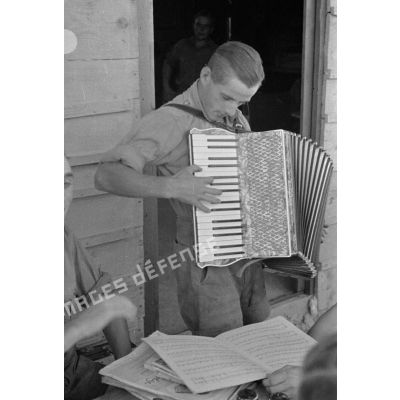 Un soldat joue de l'accordéon devant la porte du foyer (Soldatenheim).