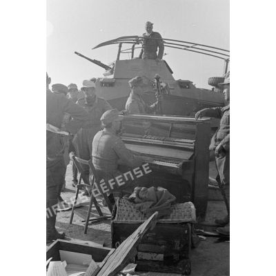 Un groupe d'officiers et de soldats allemands joue du piano et d'une contrebasse, un blindé SdKfz-232 immatriculé WH-784 231 s'est arrêté près d'eux.