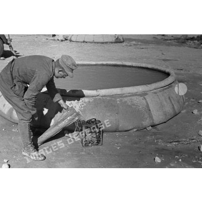 Un soldat remplit une nourrice d'eau. Cette eau a été recueillie dans un bac souple circulaire.