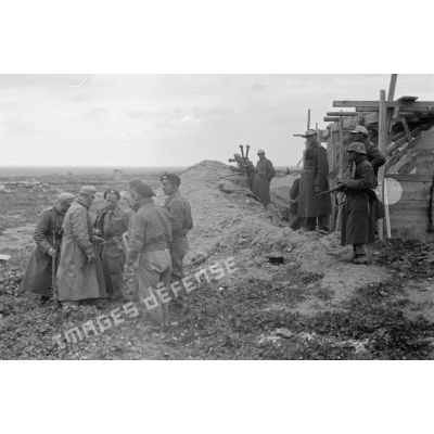 Près du parapet et d'une construction en planches, un officier allemand interroge des prisonniers britanniques.