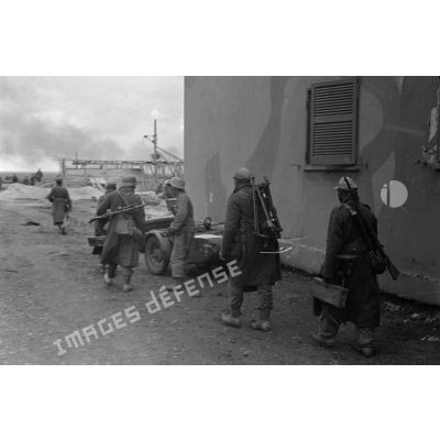 Une équipe de mitrailleurs (MG-34) passe près d'un bâtiment camouflé et d'un side-car.
