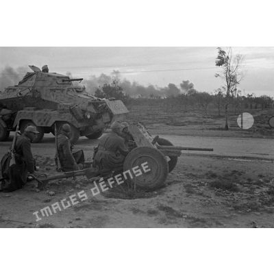 Des soldats sont accroupis près de la route derrière un canon de 3,7 cm PaK en batterie.