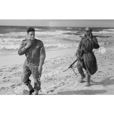 Un soldat allemand tenant une mitrailleuse MG-34 conduit un prisonnier britannique le long d'une plage.