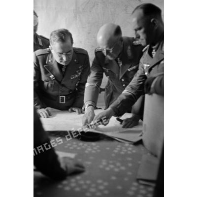 Les généraux Cavarello, Bastico, Crüwell et Gause, entourés d'autres officiers italiens et allemands, étudient une carte posée sur une table.