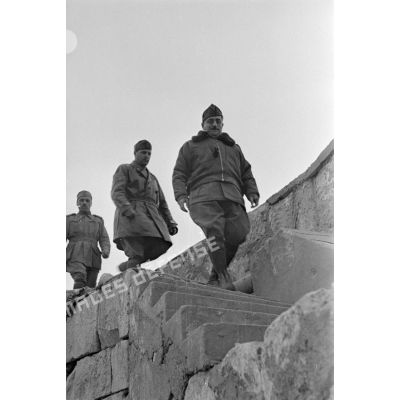 Le général Cavarello suivi de deux officiers italiens descend un escalier de pierre qui mène au port.
