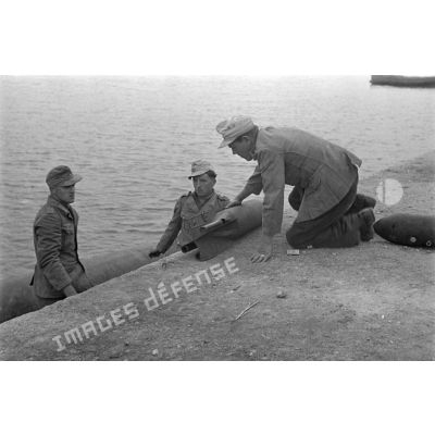 Sur le quai du port, trois soldats allemands manipulent des bombes d'aviation.