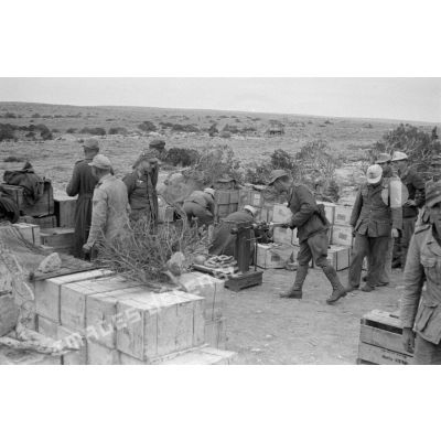 Des caisses d'approvisionnement, des soldats travaillent tandis que d'autres pèsent des aliments (saucisses).