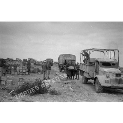 Une colonne de camions composée de camions Opel Blitz et Chevrolet, près des parcs d'approvisionnement, des soldats qui y assurent la manutention.