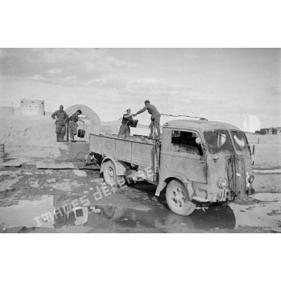 Un camion est garé près d'un puits dont des soldats italiens tirent des seaux d'eau pour remplir des barils.