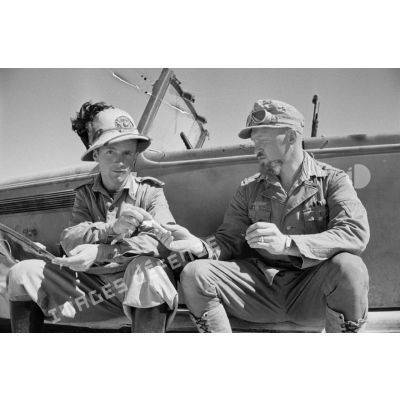Un caporal-chef (Obergefreiter) et un Bersaglier discutent et fument, assis sur le marchepied d'une voiture.