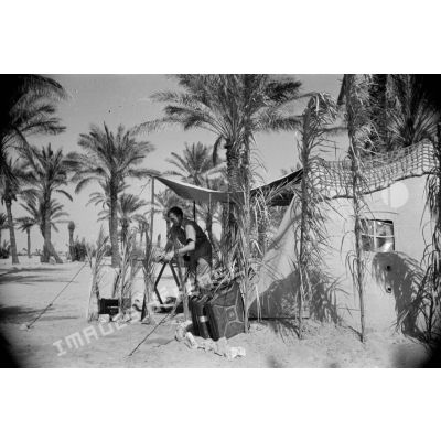 Des soldats nettoient le campement près de leur tente placée sous des palmiers.