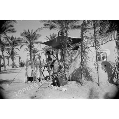 Des soldats nettoient le campement près de leur tente placée sous des palmiers.