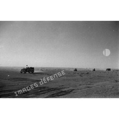 Des voitures Kfz-15 suivies de side-cars roulent dans le désert, l'une des voitures porte un fanion.