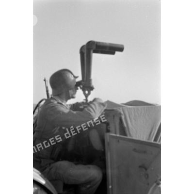 Un officier observe le terrain avec un binoculaire.