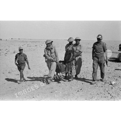 Des prisonniers transportent un blessé installé dans une couverture, gardés par deux soldats allemands armés de pistolets Walther-P-38.