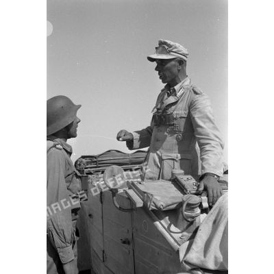 Le colonel (Oberst) Alfred Bruer commandant du Panzer-Artillerie-Regiment 155 de la 21. Panzer-Division, debout dans une voiture Kübelwagen, parle avec ses officiers.