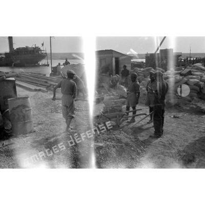 Dans le port de Tobrouk, des ouvriers et des prisonniers britanniques s'activent à la reconstruction des quais.