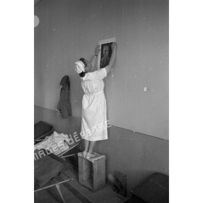 Une infirmière accroche un portrait de Rommel au mur d'une salle de l'hôpital allemand.