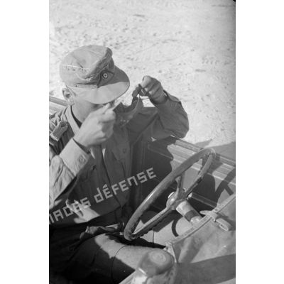 Un Sonderführer au volant d'une voiture Kübelwagen met des lunettes de protection contre le sable.